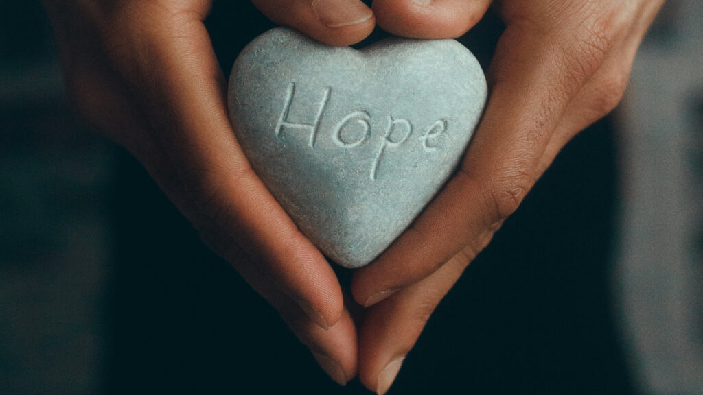 Hände halten einen Stein mit dem Wort Hope